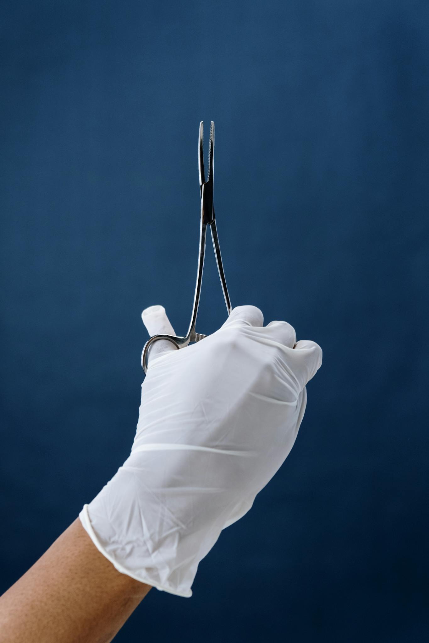 Close-up of a gloved hand holding surgical forceps vertically, ideal for medical themes.