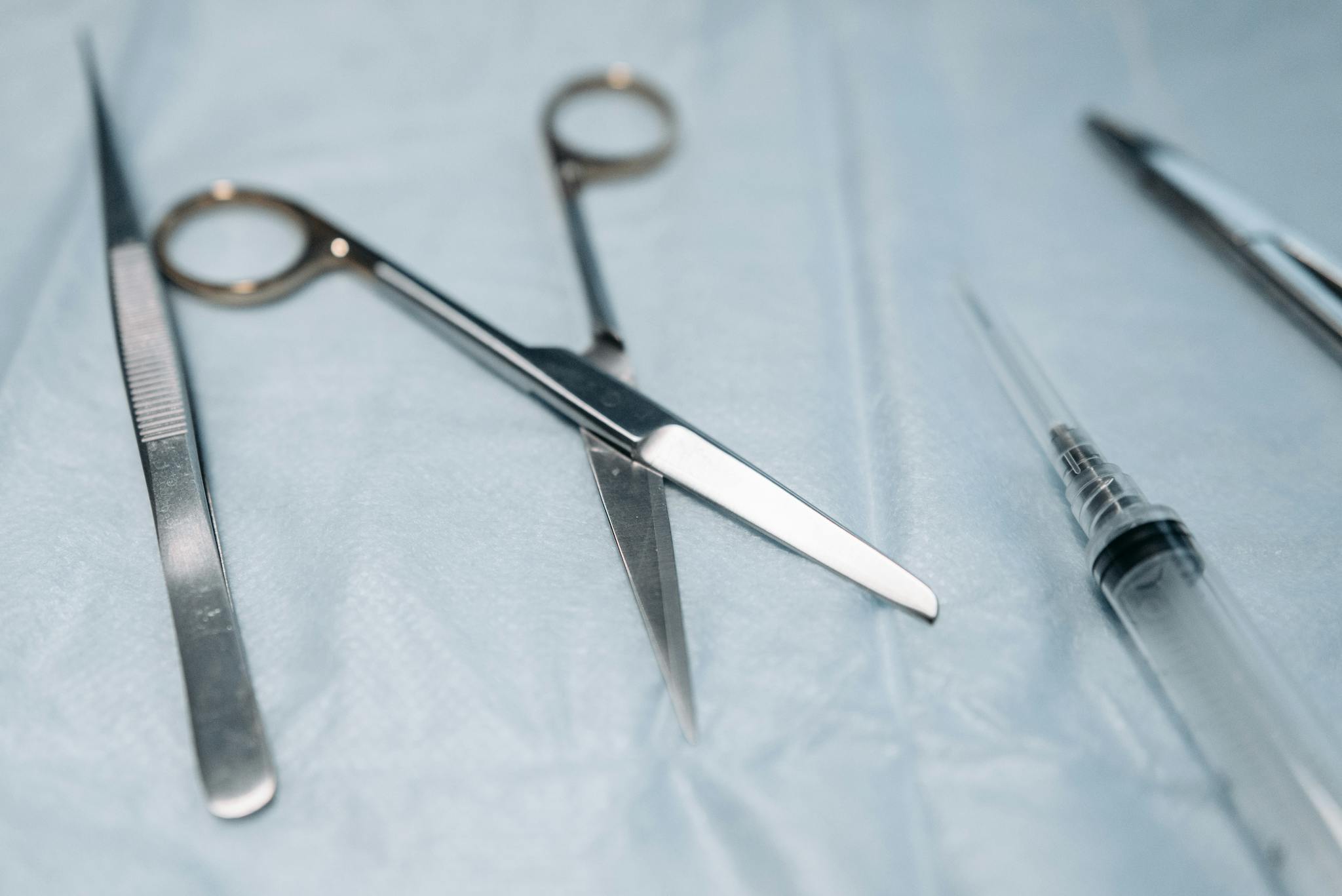Detailed view of surgical tools including scissors on a blue sterile surface.